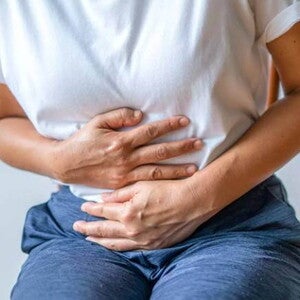 mulher com usando camiseta branca, levemente curvada e com as mãos posicionadas na barriga mulher com usando camiseta branca, levemente curvada e com as mãos posicionadas na barriga