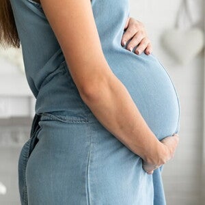 Mulher grávida de perfil com as mãos sobre a barriga