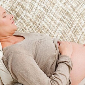 Mulher grávida deitada no sofá embalando sua barriga Mulher grávida deitada no sofá embalando sua barriga