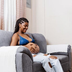 mulher grávida sentada ao sofá enquanto sente contração do bebê