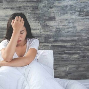 mulher sentada em cama com lençóis brancos enquanto está cabisbaixa. mulher sentada em cama com lençóis brancos enquanto está cabisbaixa.
