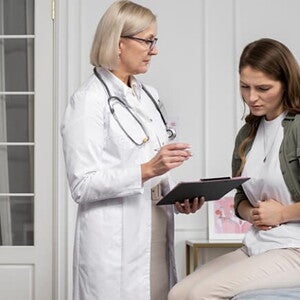 Mulher sentada em uma cama de hospital discutindo sua condição médica com uma profissional de saúde Mulher sentada em uma cama de hospital discutindo sua condição médica com uma profissional de saúde