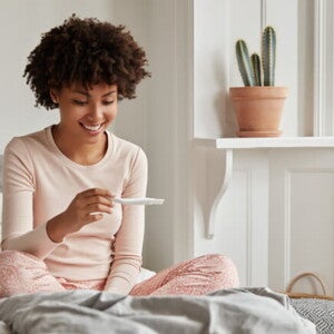 Mulher sentada na cama olhando feliz para um teste de gravidez Mulher sentada na cama olhando feliz para um teste de gravidez