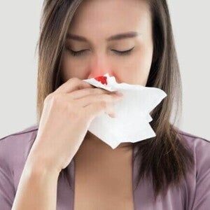 Mulher grávida com os olhos fechados, segurando um lenço de papel para estancar um sangramento no nariz. O lenço está com uma mancha de sangue. A imagem mostra a condição de nariz sangrando na gravidez.