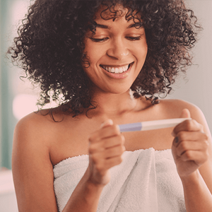 Smiling woman wrapped in a towel looking at a pregnancy test.