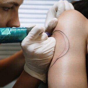 Detalhe de um tatuador fazendo um contorno de tatuagem no braço de outra pessoa.