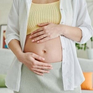 Uma gestante em pé em uma sala, com as mãos sobre a barriga. Uma gestante em pé em uma sala, com as mãos sobre a barriga.