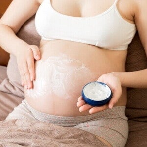 Gestante aplicando creme hidratante suave na barriga para acalmar a pele e reduzir a irritação.