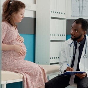 Gestante sentada sobre uma maca conversa com um médico sentado na sua frente Gestante sentada sobre uma maca conversa com um médico sentado na sua frente