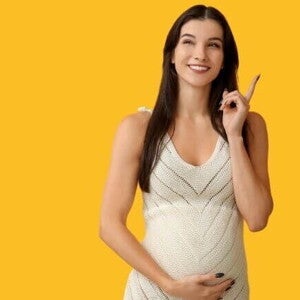 Mulher grávida sorridente, apontando para cima com o dedo. Ela usa um vestido branco e está de frente para um fundo amarelo. A imagem sugere a descoberta e o esclarecimento sobre os tipos de tampão mucoso durante a gravidez.