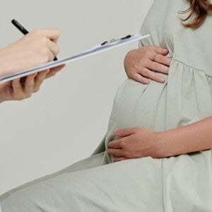 Um médico faz anotações em uma prancheta enquanto uma mulher grávida está sentada em uma cadeira Um médico faz anotações em uma prancheta enquanto uma mulher grávida está sentada em uma cadeira