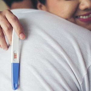 Uma mulher abraçando o marido enquanto segura um teste de gravidez Uma mulher abraçando o marido enquanto segura um teste de gravidez