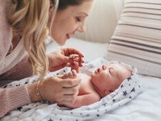mãe sorrindo e brincando com o bebê recém-nascido na cama.
