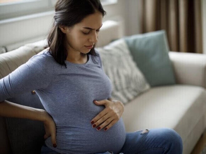 Mulher grávida com náusea, sentada no sofá