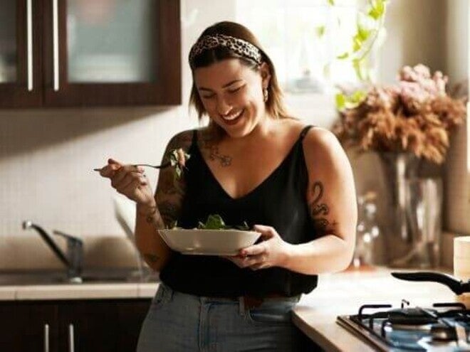 Mulher sorrindo e comendo salada na cozinha