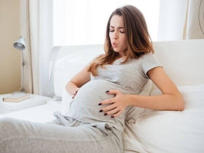 Mulher grávida deitada na cama, com as mãos na barriga e uma expressão de desconforto. A imagem ilustra o momento de sentir as contrações de treinamento, uma das sensações comuns durante a gestação. Mulher grávida deitada na cama, com as mãos na barriga e uma expressão de desconforto. A imagem ilustra o momento de sentir as contrações de treinamento, uma das sensações comuns durante a gestação.