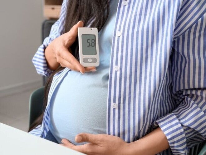 Imagem de uma gestante segurando um glicosímetro com uma mão enquanto a outra mão está sustentando a parte inferior da barriga, simbolizando a atenção em relação à diabetes gestacional.
