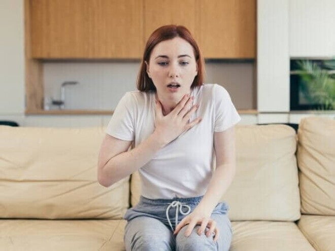 Mulher sentada em um sofá com uma das mãos sobre o pescoço e a boca levemente aberta Mulher sentada em um sofá com uma das mãos sobre o pescoço e a boca levemente aberta