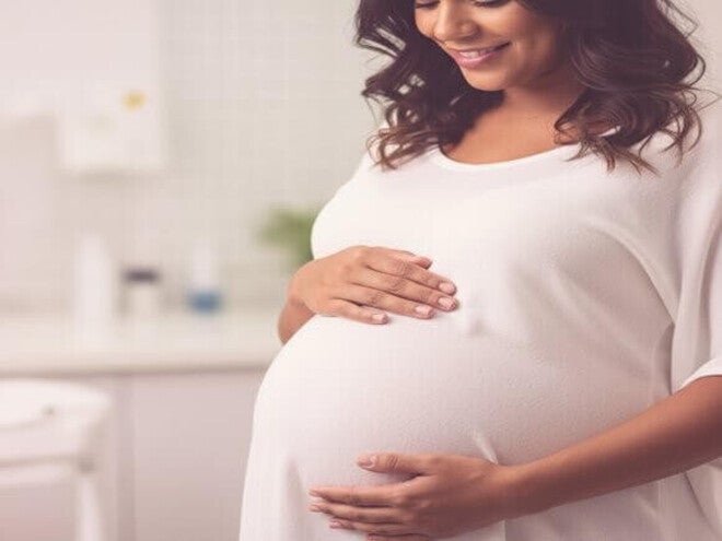 Mulher grávida mixed-race no terceiro trimestre tocando a barriga gentilmente, representando exames finais e parto.