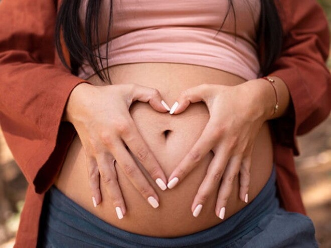 Gestante com as mãos sobre a barriga fazendo o formato de um coração com as mãos Gestante com as mãos sobre a barriga fazendo o formato de um coração com as mãos