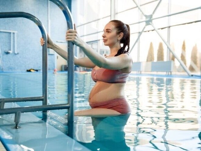 Mulher grávida praticando exercícios leves dentro de uma piscina Mulher grávida praticando exercícios leves dentro de uma piscina