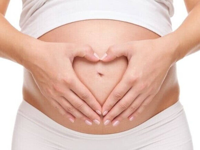 Close de mulher grávida com as mãos formando um coração sobre a barriga.