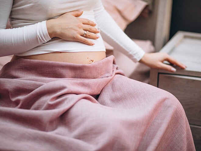 mulher grávida sentada na cama com a mãe na barriga 
