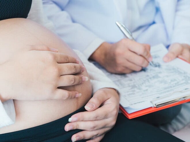Médico com uma prancheta nas mãos fazendo anotações enquanto uma mulher grávida está sentada na cama Médico com uma prancheta nas mãos fazendo anotações enquanto uma mulher grávida está sentada na cama