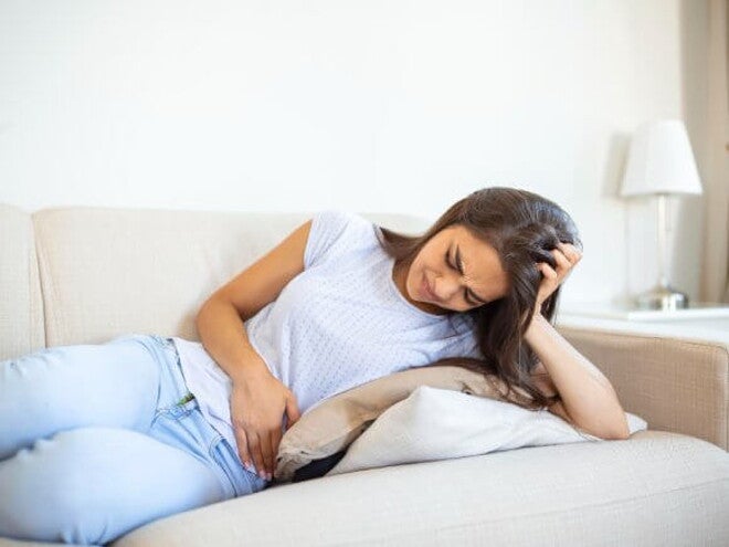 mulher com blusa branca deita no sofá sentindo cólicas abdominais mulher com blusa branca deita no sofá sentindo cólicas abdominais