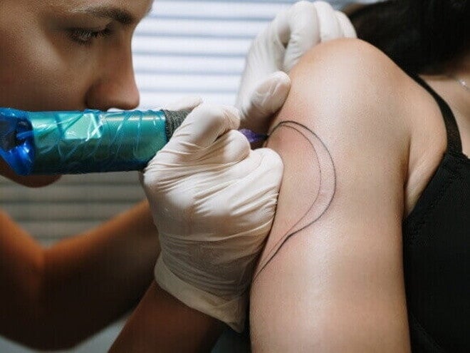 Detalhe de um tatuador fazendo um contorno de tatuagem no braço de outra pessoa.