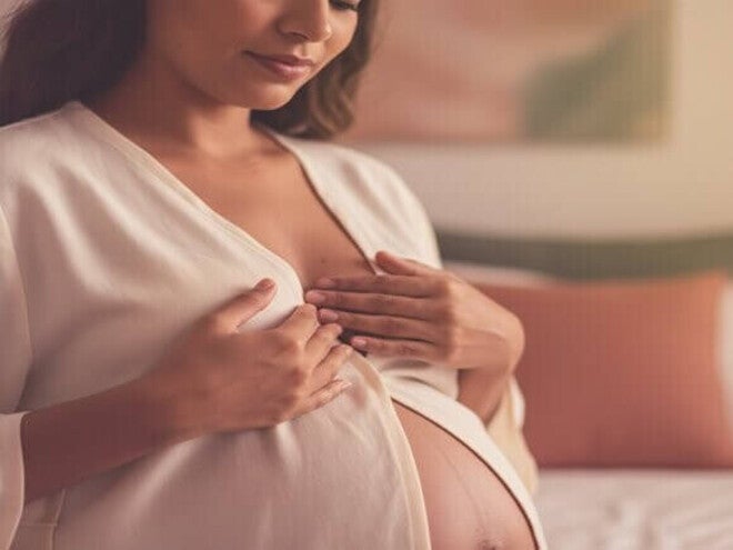 Mulher grávida diversificada tocando o seio, preparando-se suavemente para a amamentação.