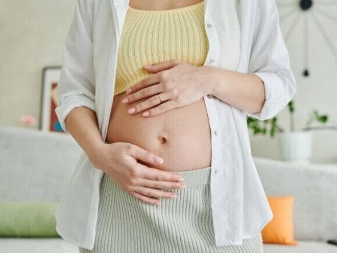 Uma gestante em pé em uma sala, com as mãos sobre a barriga. Uma gestante em pé em uma sala, com as mãos sobre a barriga.