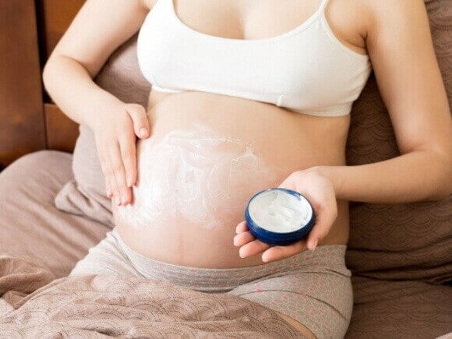 Gestante aplicando creme hidratante suave na barriga para acalmar a pele e reduzir a irritação.