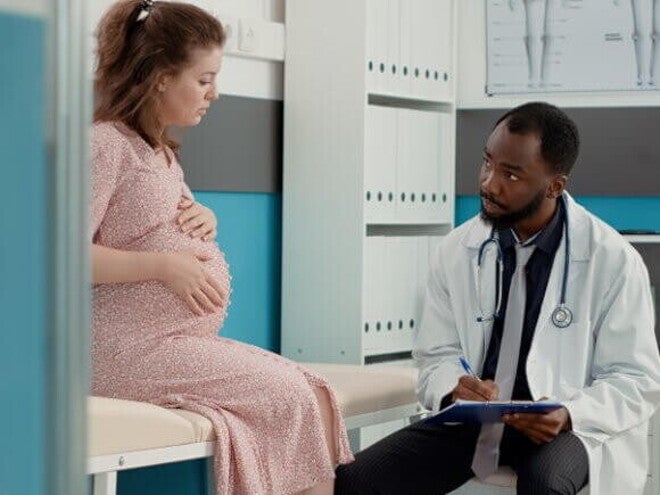 Gestante sentada sobre uma maca conversa com um médico sentado na sua frente Gestante sentada sobre uma maca conversa com um médico sentado na sua frente