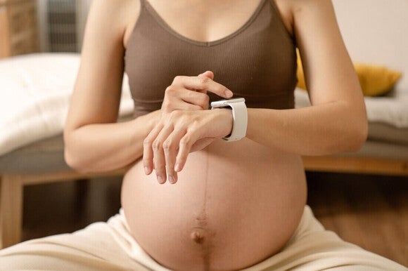 Mulher grávida sentada em um tapete de exercícios, cronometrando as contrações