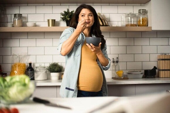 Mulher grávida com SOP na cozinha tomando um café da manhã nutritivo.