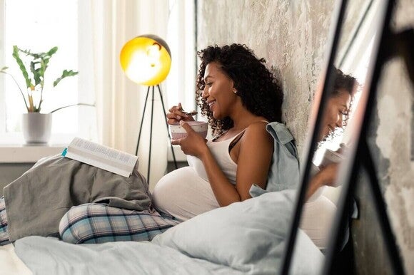 Mulher grávida sentada na cama comendo um lanche salgado