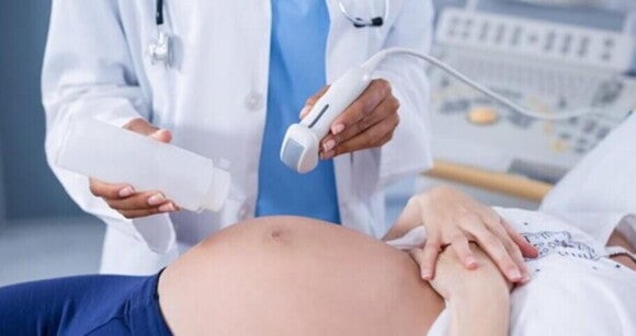 Mulher grávida deitada realizando exame de ultrassonografia Mulher grávida deitada realizando exame de ultrassonografia