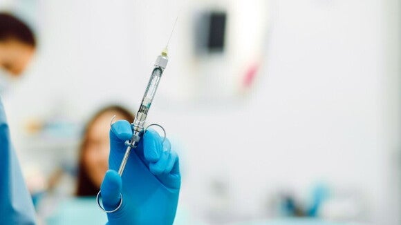 Mão com luva segurando uma injeção para aplicar a anestesia peridural em um centro cirúrgico. Mão com luva segurando uma injeção para aplicar a anestesia peridural em um centro cirúrgico.