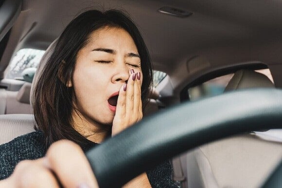 Mulher bocejando enquanto dirige um carro