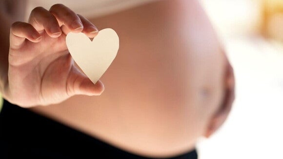 Gestante segurando um coração de papel sobre a barriga, ilustrando a motivação e o cuidado necessários para parar de fumar na gravidez e proteger a saúde fetal.