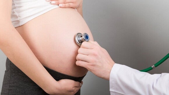 Profissional de saúde auscultando a barriga de uma gestante com estetoscópio para monitorar a saúde do bebê.