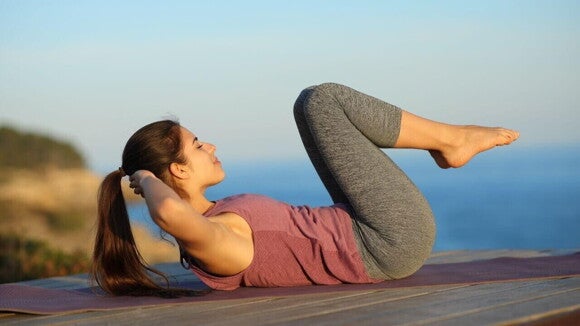 Uma mulher deitada em um espaço ao ar livre, fazendo um exercício abdominal Uma mulher deitada em um espaço ao ar livre, fazendo um exercício abdominal