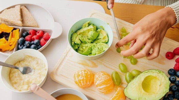 Mãos preparando uma refeição com muitas frutas, ilustrando o preparo de alimentos seguros e saudáveis para a mãe que segue uma dieta APLV.