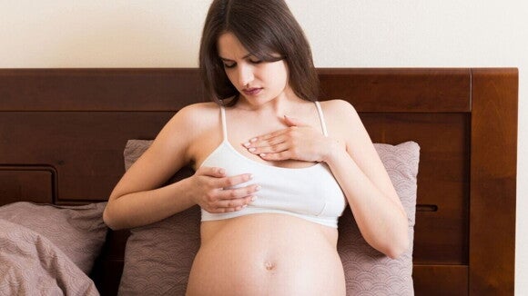 Mulher grávida com uma expressão de desconforto, segurando o peito, exemplificando a dor nos seios na gravidez.