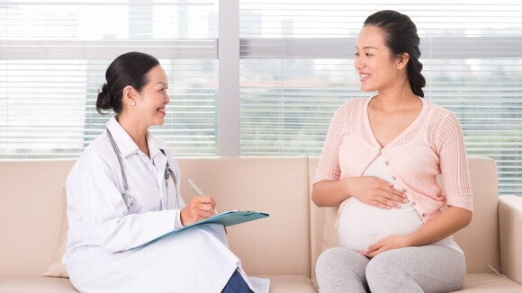 Consulta médica para monitoramento da gravidez, mostrando uma gestante sorridente sentada ao lado de uma médica.