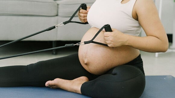 Grávida fazendo exercício com faixa elástica sentada no tapete. Grávida fazendo exercício com faixa elástica sentada no tapete.