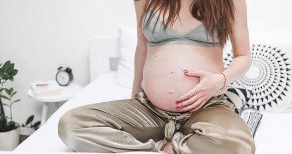 Mulher grávida usando pijamas sentada na cama e acariciando a barriga. Mulher grávida usando pijamas sentada na cama e acariciando a barriga.