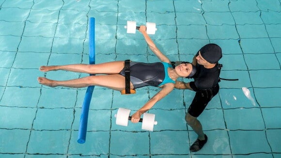 Mulher grávida praticando exercícios suaves em uma piscina, acompanhada por profissional de saúde, demonstrando alívio e bem-estar durante sessão de hidroterapia. Mulher grávida praticando exercícios suaves em uma piscina, acompanhada por profissional de saúde, demonstrando alívio e bem-estar durante sessão de hidroterapia.