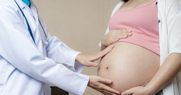 Imagem de um profissional da saúde colocando as mãos em cima da barriga de uma mulher grávida Imagem de um profissional da saúde colocando as mãos em cima da barriga de uma mulher grávida